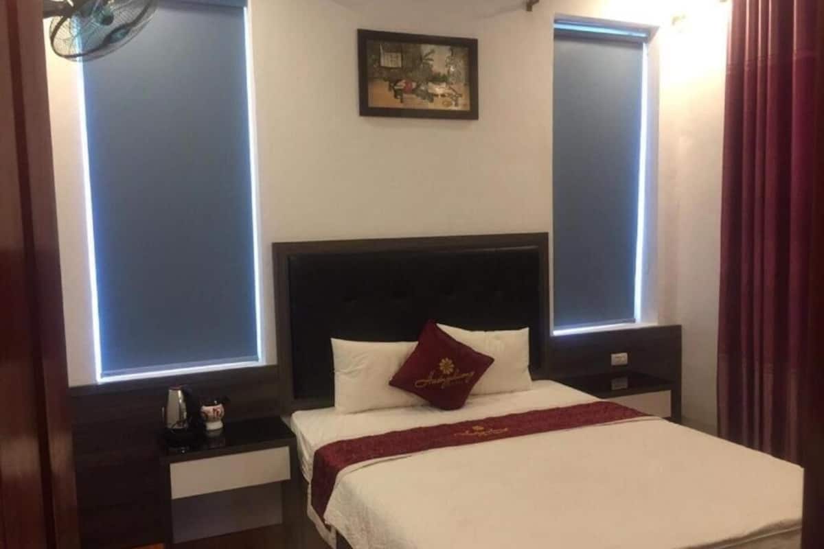 Une chambre d’hôtel comprenant un lit, une table de chevet, une commode, une fenêtre avec des rideaux et un tableau accroché au mur.