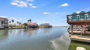 A waterfront property with a dock, a covered area with chairs, and a house with a red roof. - Relaxing Waterfront Home on Laguna Madre- Near Beach with Kayaking and Nature (Corpus Christi)