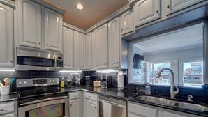 A modern kitchen with white cabinetry, stainless steel appliances, and a large window providing a view of the city. - Relaxing Waterfront Home on Laguna Madre- Near Beach with Kayaking and Nature (Corpus Christi)