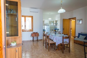 Un comedor con una mesa de madera dispuesta para cuatro personas, un aparador con puertas de vidrio y un sofá al fondo.