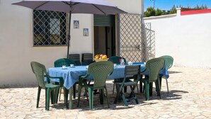 Une terrasse extérieure avec une table et des chaises, un parasol et une fenêtre donnant sur un paysage agréable.
