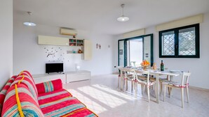 Un salon moderne comprenant un canapé, un téléviseur, une table à manger, des chaises et une fenêtre.