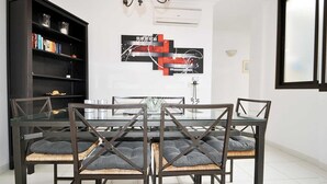 Un coin repas avec une table à plateau en verre, quatre chaises dotées d’assises rembourrées, une bibliothèque noire et un tableau moderne abstrait accroché au mur.