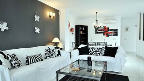Un salon moderne avec un canapé blanc, des coussins à motifs noir et blanc, une table basse en verre et un tapis noir.