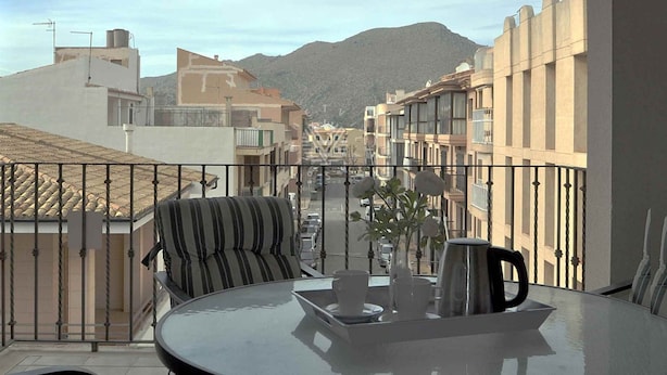 Un balcon avec une table, des chaises et une vue sur une rue et des montagnes.