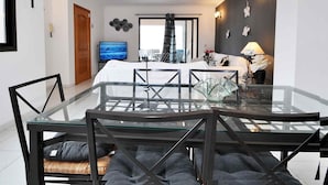 Une chambre d’hôtel moderne avec une table à manger en verre, un lit recouvert d’une couette blanche, une télévision et une vue sur la ville.