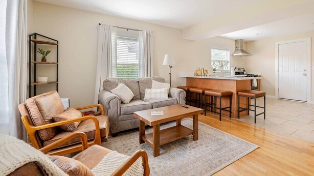 A living room with a sofa, coffee table, and chairs, a kitchen area with a bar, and a door.