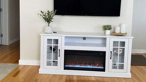 A living room with a white entertainment center, a flat-screen TV mounted above it, and a fireplace below.
