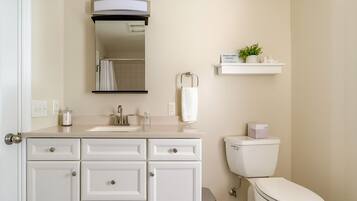 Une salle de bain moderne avec un meuble-lavabo blanc, un évier, un miroir, des toilettes et une petite étagère sur laquelle est posée une plante.