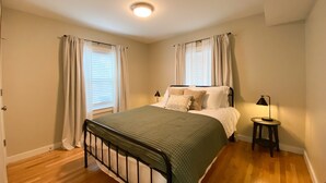 A bedroom with a bed, two bedside tables, a window with curtains, and a ceiling light.