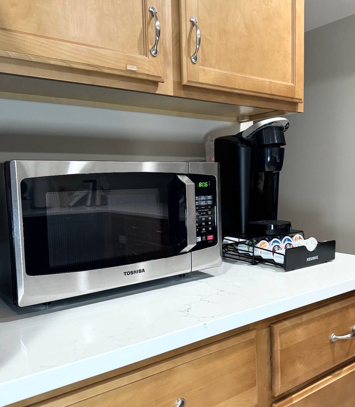 Una cocina con microondas de acero inoxidable, cafetera y armarios de madera.