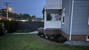 A residential backyard with a lawn, a brick planter, and a house with a porch.