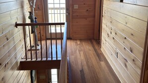Un couloir intérieur aux murs en bois, avec une porte en bois, une petite fenêtre et un luminaire au plafond.