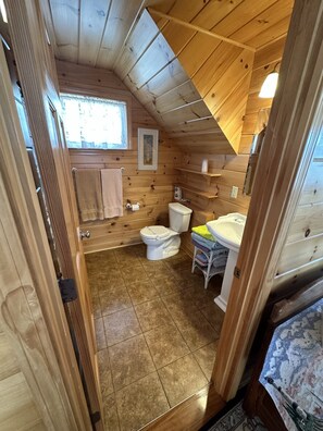 A compact wooden cabin bathroom with a toilet, sink, and shower area. - 4 Bedroom Oceanfront Cottage on Old Orchard Beach (Old Orchard Beach)