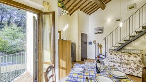 A dining area with a table set for four, a sofa, and a staircase. - Tuscan Sun Duplex with Balcony and Shared Pool, Radicondoli, Italy (Radicondoli)