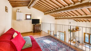 A spacious room with a high ceiling, wooden beams, a red sofa, a patterned rug, a television, and a balcony with a railing. - Tuscan Sun Duplex with Balcony and Shared Pool, Radicondoli, Italy (Radicondoli)