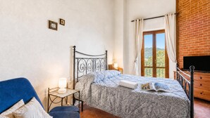 A bedroom with a bed, a nightstand, a lamp, a chair, a window with curtains, and a TV. - Tuscan Sun Duplex with Balcony and Shared Pool, Radicondoli, Italy (Radicondoli)