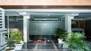 A modern lobby with a glass partition, potted plants, and a car parked inside. - Shaan Stay (Gurugram)