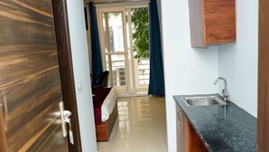 A hallway leading to a bedroom with a window, a bathroom with a sink, and a wooden door. - Shaan Stay (Gurugram)