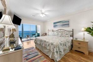 A bedroom with a bed, bedside tables, a TV, and a view of the ocean. - Regency Towers Penthouse #1409 (Panama City Beach)