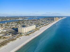 An aerial view of a coastal city with a long sandy beach, a large hotel with multiple floors, and a clear blue ocean. - Regency Towers Penthouse #1409 (Panama City Beach)