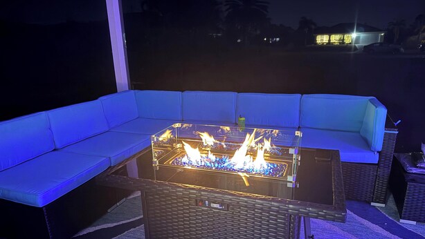 A glass-top fire feature with a metal frame, a blue cushioned sofa, and a wicker table. - Cozy and Economical Vacation Rental (Cape Coral)