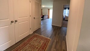 A hallway with a patterned rug, white doors, and a view into a living area with a sofa and a window. - Cozy and Economical Vacation Rental (Cape Coral)