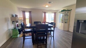 A dining area with a table and chairs, a green side table, a cabinet with glass doors, and a refrigerator. - Cozy and Economical Vacation Rental (Cape Coral)