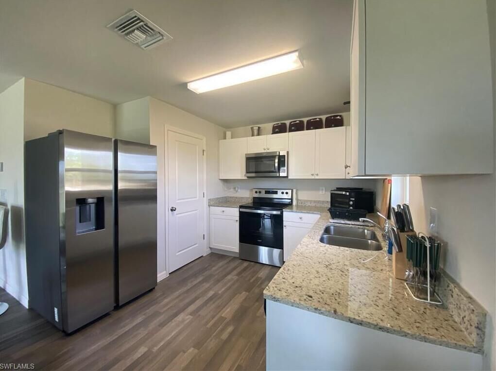 A modern kitchen with stainless steel appliances, white cabinetry, and a granite countertop.