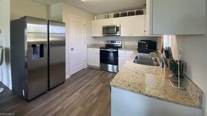 A modern kitchen with stainless steel appliances, white cabinetry, and a granite countertop. - Cozy and Economical Vacation Rental (Cape Coral)
