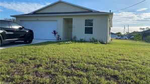 A single-story house with a garage, a small front yard, and a clear blue sky. - Cozy and Economical Vacation Rental (Cape Coral)