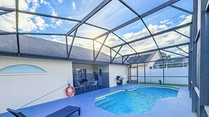 A covered outdoor swimming pool with lounge chairs and a barbecue area. - Modern Home w/Pool close to Disney Florida theme parks (Kissimmee)