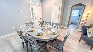 A dining area with a round table set for six, surrounded by chairs. There are two doors in the background, one leading to a hallway and the other to a room. - Modern Home w/Pool close to Disney Florida theme parks (Kissimmee)