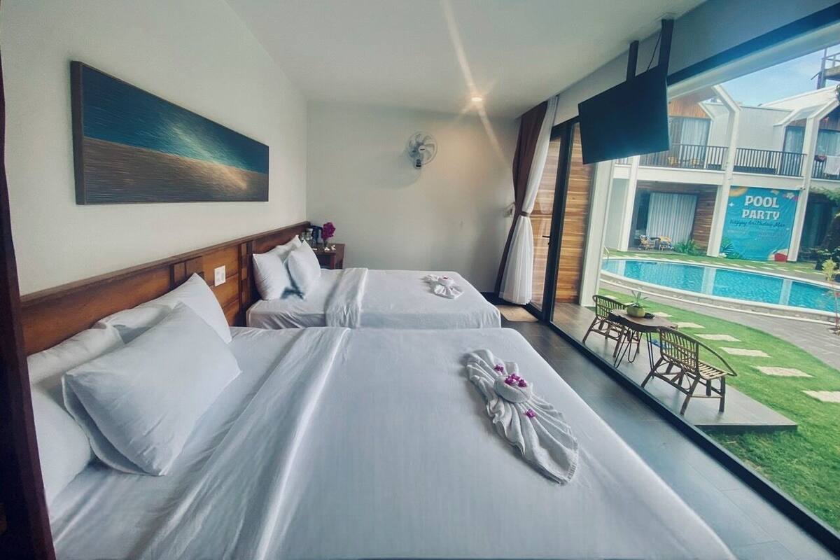 A hotel room with two beds, a view of a pool, and a balcony with outdoor furniture.