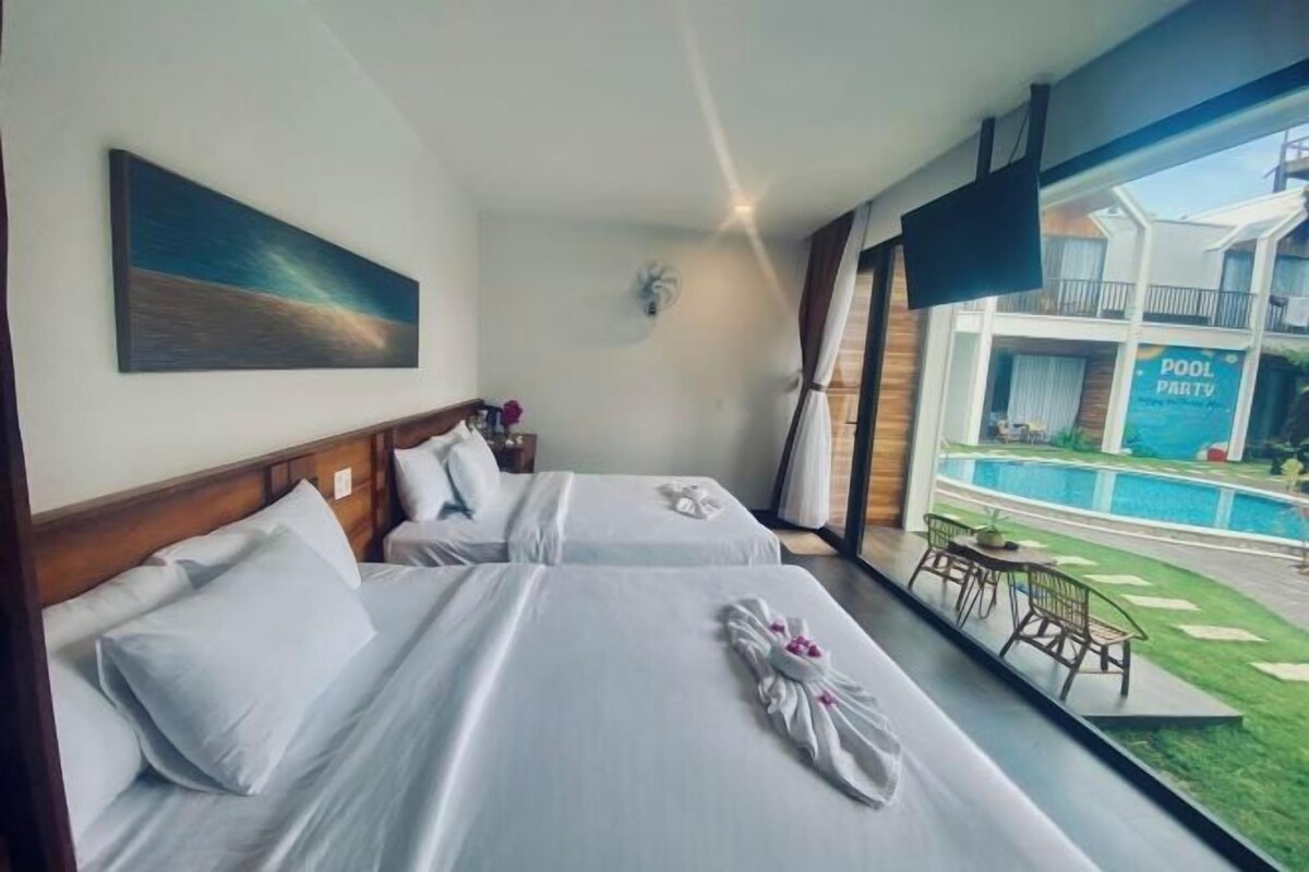 Habitación de hotel con dos camas, un cuadro en la pared, vista a un área de piscina y una mesa con sillas afuera.