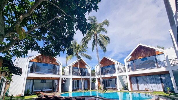 Un resort moderno con piscina, zonas de descanso y un entorno tropical con palmeras.