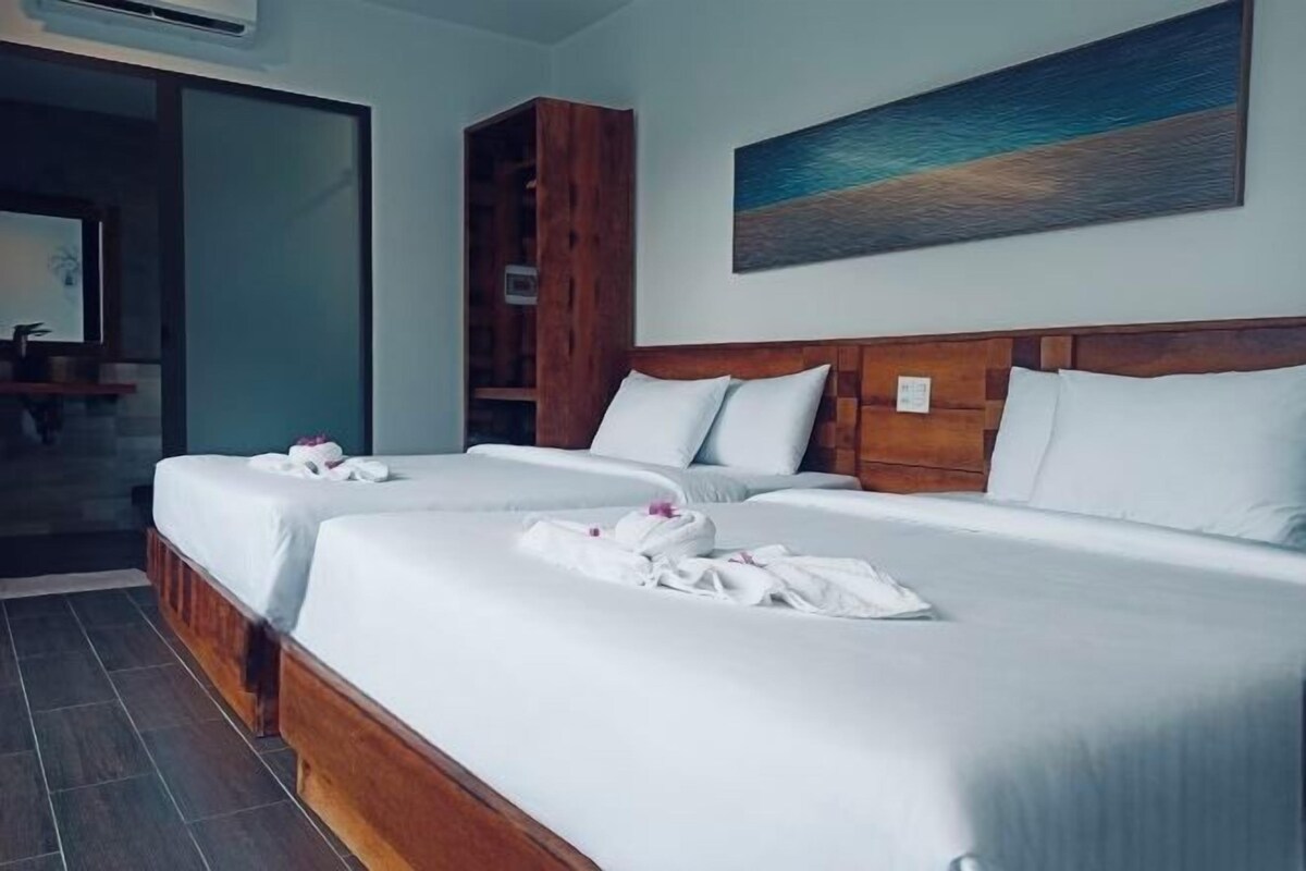 A hotel room with two beds, wooden headboards, white linens, and a painting of a beach.