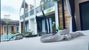 Habitación de hotel con cama, vista a la piscina y balcón con plantas.