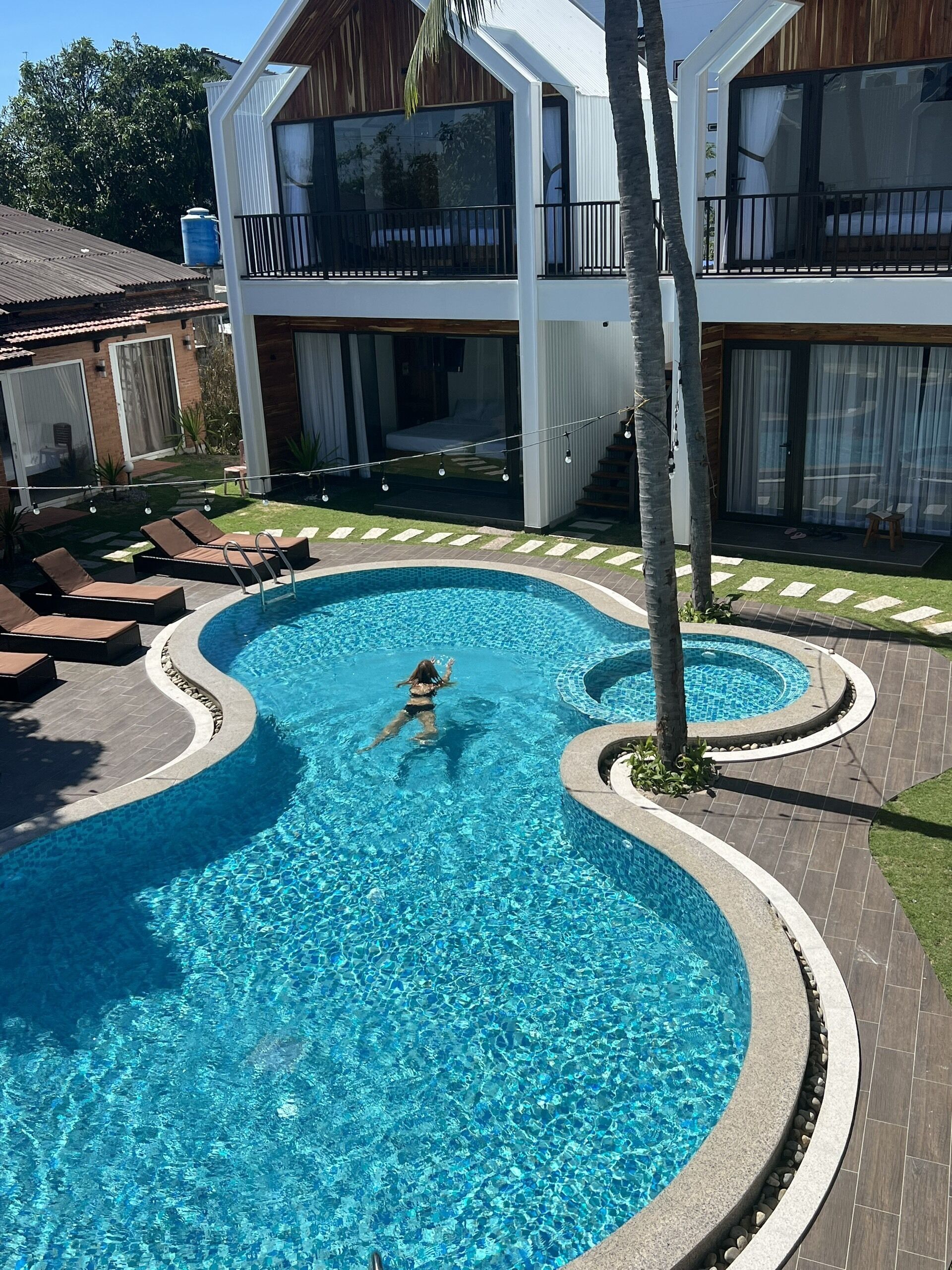 A swimming pool with a curved design, surrounded by lounge chairs and a small deck area.
