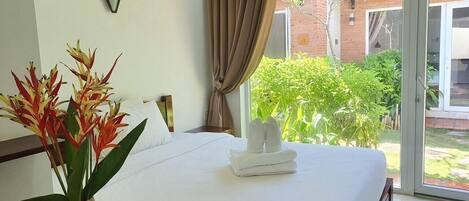 Una habitación de hotel con una cama, un jarrón con flores y vistas a la vegetación.