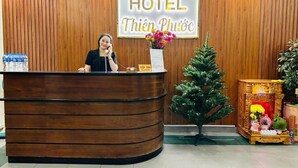 A hotel reception desk with a wooden panel wall, clocks displaying different cities, and a Christmas tree. - Thien Phuoc Hotel - by Bay Luxury (Ho Chi Minh City)