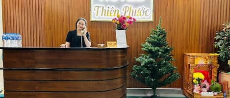 A hotel reception desk with a wooden panel wall, clocks displaying different cities, and a Christmas tree.