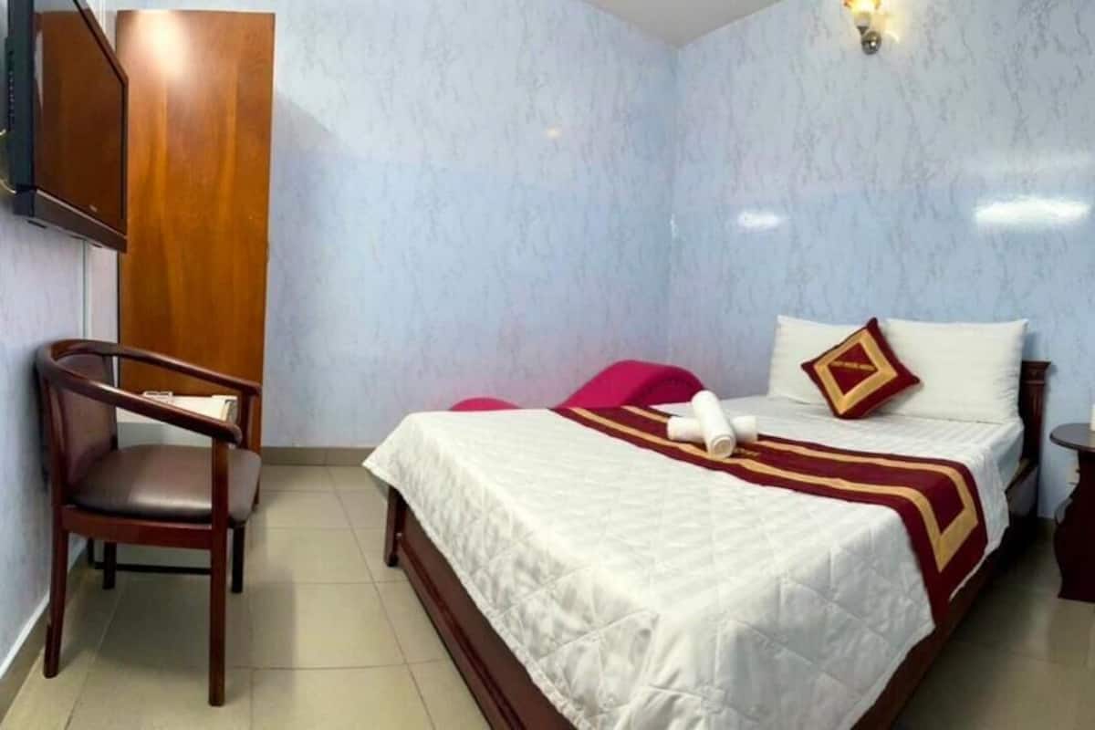 Habitación de hotel con cama, una silla, televisor montado en la pared y una mesita con un florero.