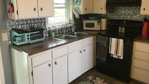 A compact kitchen with white cabinets, a black stove, a microwave, and a toaster. - Cozy lake house on Sabattus Pond 2 bed 1 Bath  (Sabattus)