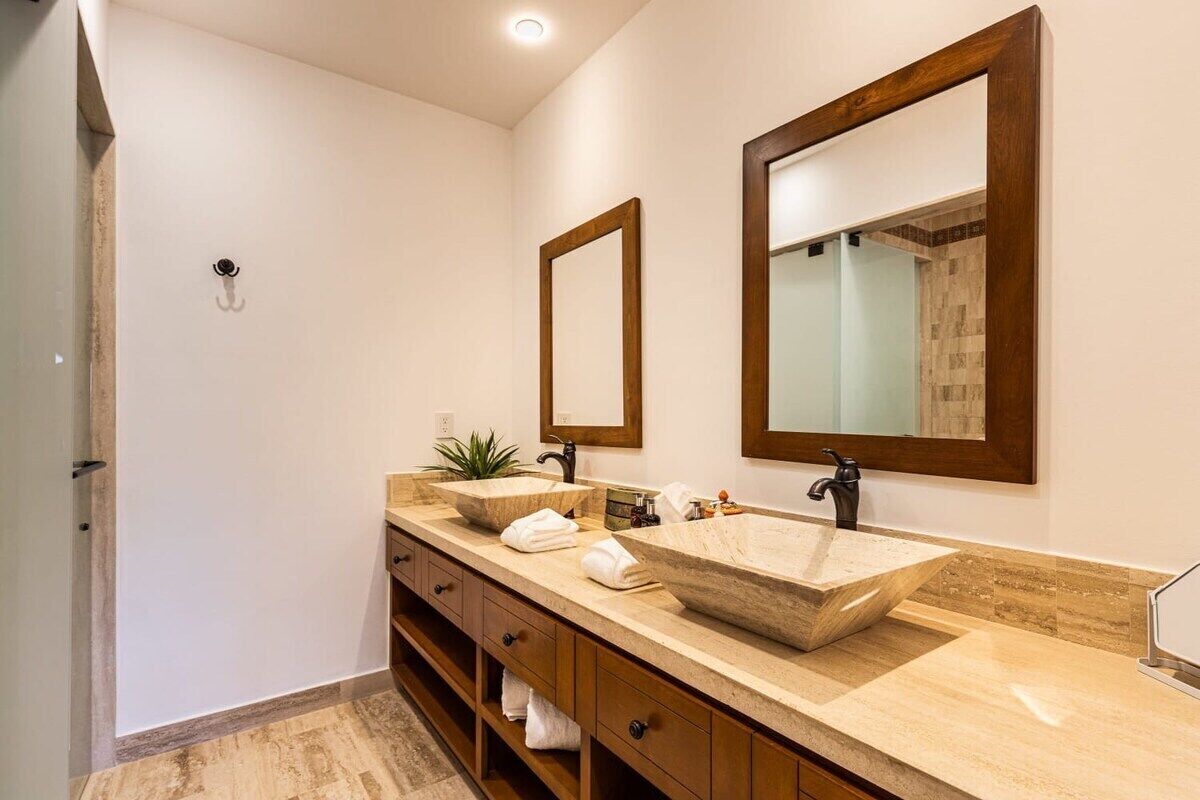 A modern bathroom with a large vessel sink, two mirrors, and a wooden vanity with drawers.
