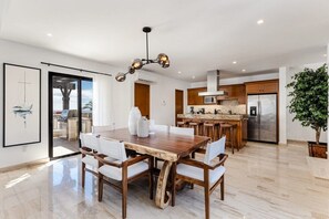 Eine moderne Küche mit einer zentralen Kochinsel, Edelstahlgeräten und einem Essbereich mit Holztisch und weißen Stühlen.