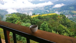 A view from a balcony with a cup on the railing, overlooking a lush valley with green hills and a thatched roof structure. - MONG NGUA BUNGALOW & HOMESTAY (Thong Nguyen)