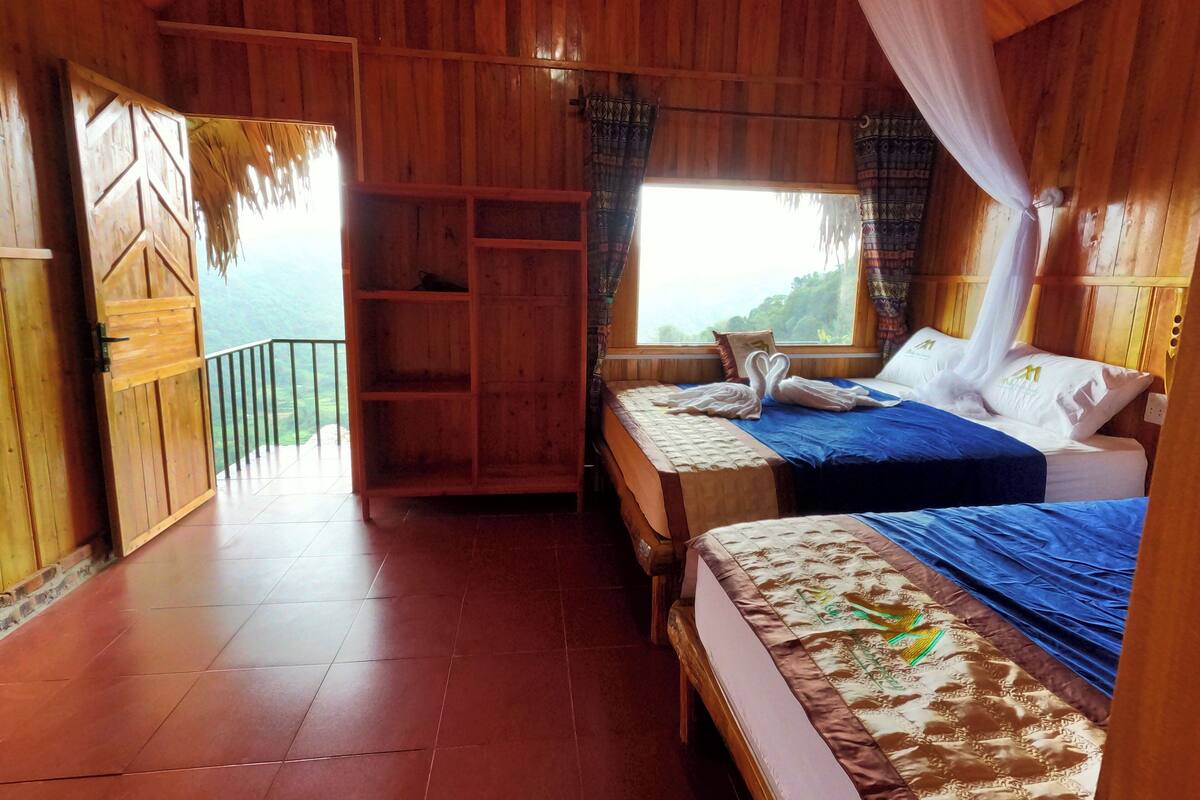 A wooden room with two beds, a wooden wardrobe, and a balcony with a view.