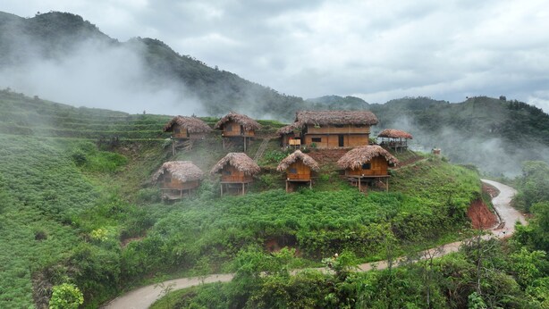 A cluster of traditional thatched-roof houses on a hillside with a winding path. - MONG NGUA BUNGALOW & HOMESTAY (Thong Nguyen)