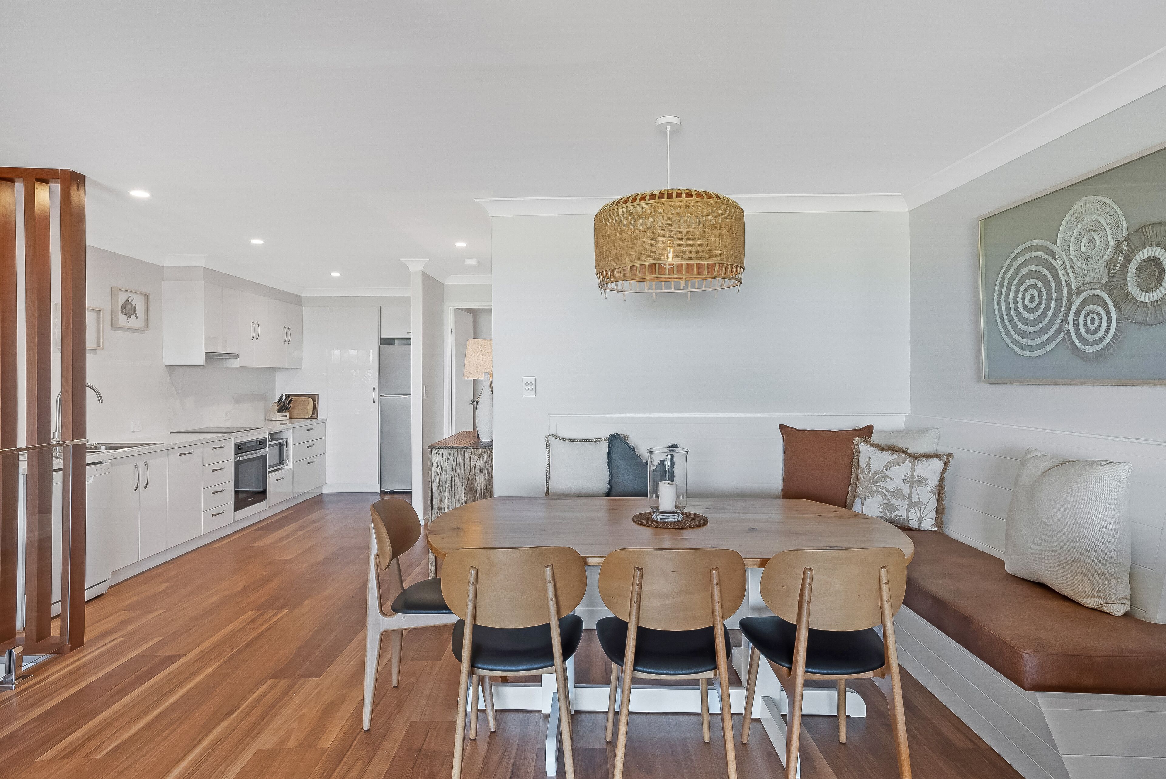 Een moderne keuken met witte kastjes, een houten eettafel met zes stoelen en een hanglamp.